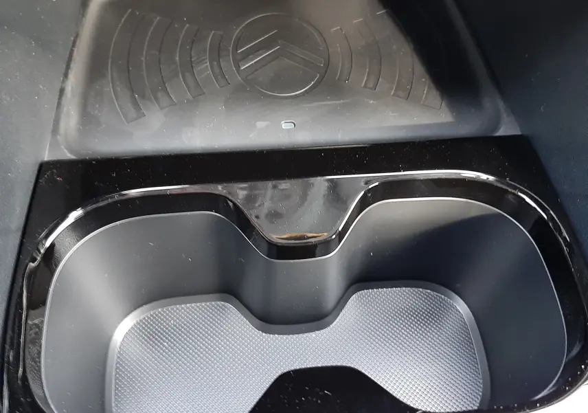 Gros plan sur le porte-gobelets noir et le chargeur à induction avec logo Citroën dans l'habitacle du C3 Aircross hybride.