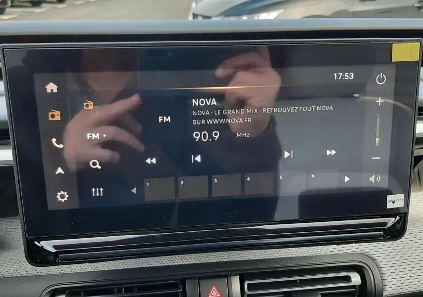 Écran tactile central affichant la radio FM sur Citroën C3 Aircross hybride 2026, intérieur noir avec commandes climatisation visibles.