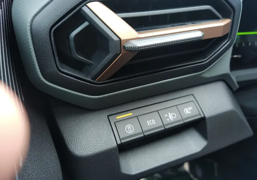 Gros plan sur la commande ECO et les boutons de réglage sous la sortie d'air au design hexagonal cuivré du tableau de bord Dacia Bigster.