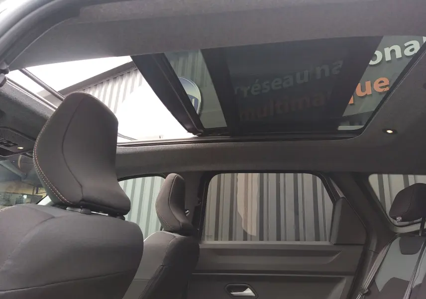 Vue intérieure arrière du Dacia Bigster gris schiste 2025, mettant en valeur le toit panoramique et les sièges noirs avec surpiqûres rouges.