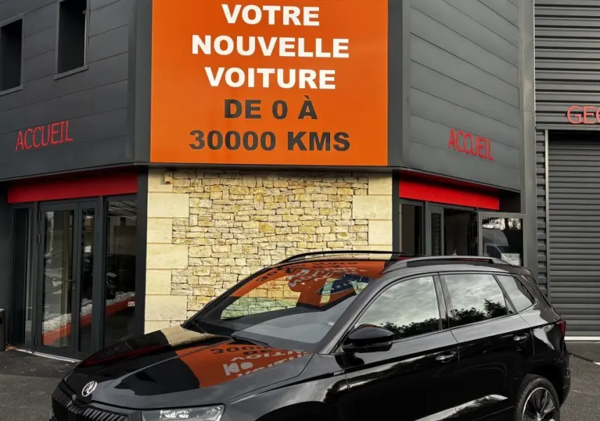 SKODA KAROQ noir vue 3/4 avant droit, garée devant un bâtiment avec panneau orange Distinxion.