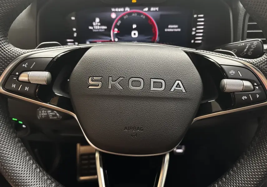 Gros plan sur le volant noir SKODA avec commandes intégrées et tableau de bord numérique en arrière-plan.