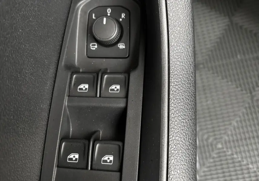 Gros plan sur les commandes noires des vitres électriques et rétroviseurs côté conducteur d'un Skoda Karoq noir 2025.