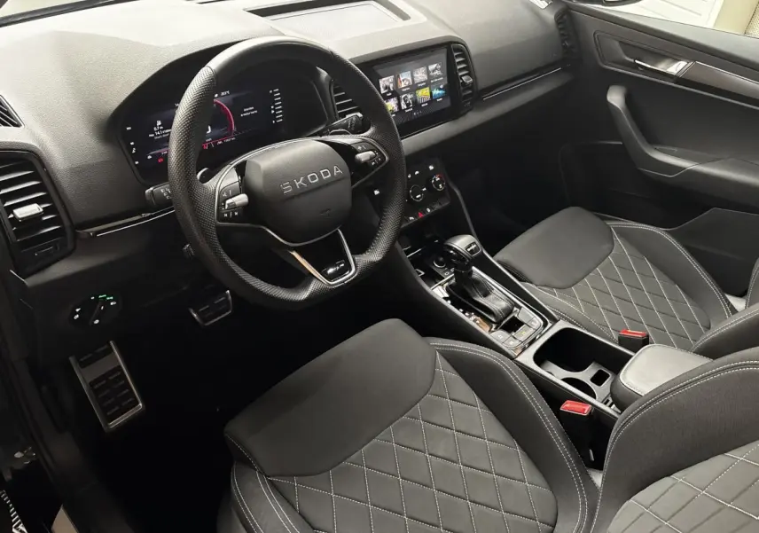 Vue intérieure côté conducteur du Skoda Karoq 2025 noir, avec volant cuir, sièges noirs matelassés et écran tactile central.