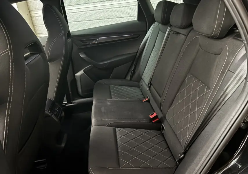 Vue côté droit de la banquette arrière noire du Skoda Karoq 2025 avec surpiqûres et ceintures rouges visibles.