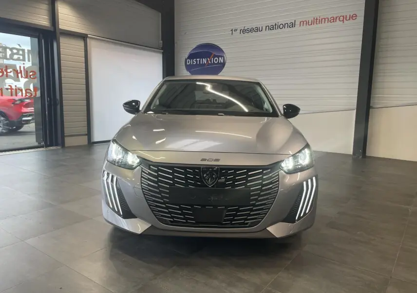 Vue frontale d'une Peugeot 208 1.2i Hybrid gris Artense avec phares LED et calandre noire brillante en showroom.