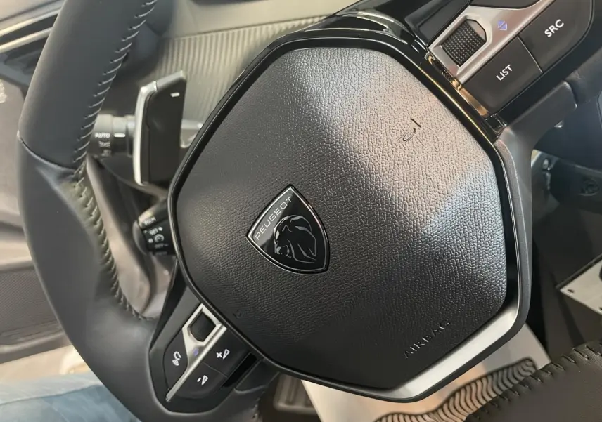 Gros plan sur le volant cuir noir du Peugeot 208 2025 avec logo lion et commandes intégrées.