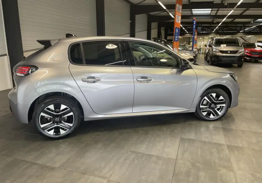 Profil côté gauche d'une Peugeot 208 1.2i Hybrid gris Artense avec jantes alliage bi-tons en showroom.