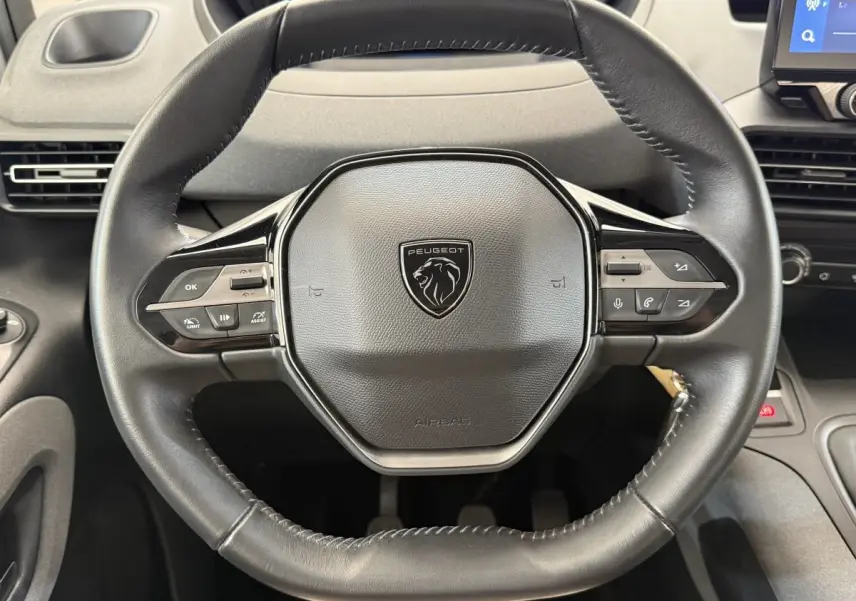 Vue rapprochée du volant cuir multifonctions noir du Peugeot Rifter 2024, avec commandes intégrées visibles.
