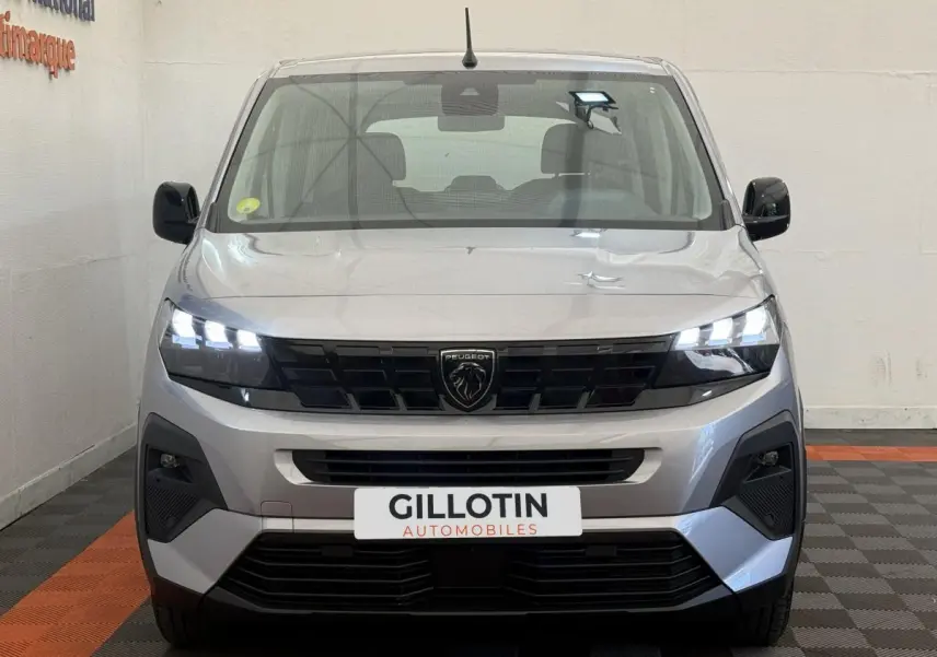 Vue frontale d'un Peugeot Rifter gris clair 2024 avec phares LED allumés et calandre noire distinctive.