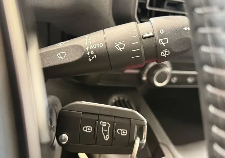 Gros plan intérieur sur la commande des essuie-glaces et la clé de contact du Peugeot Rifter gris clair 2024.