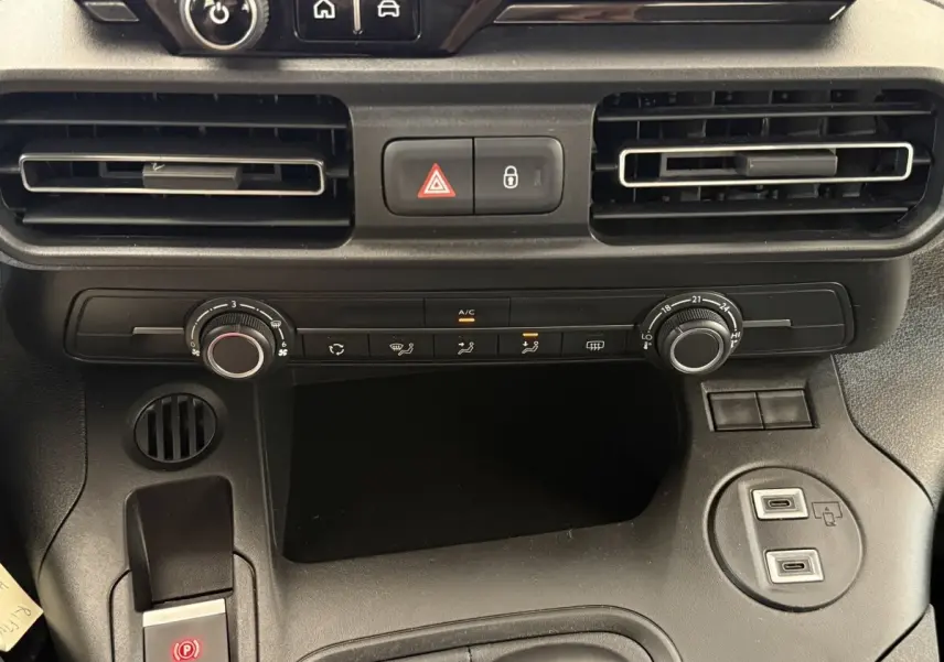 Gros plan sur la console centrale du Peugeot Rifter gris clair 2024, avec commandes climatisation et ports USB visibles.