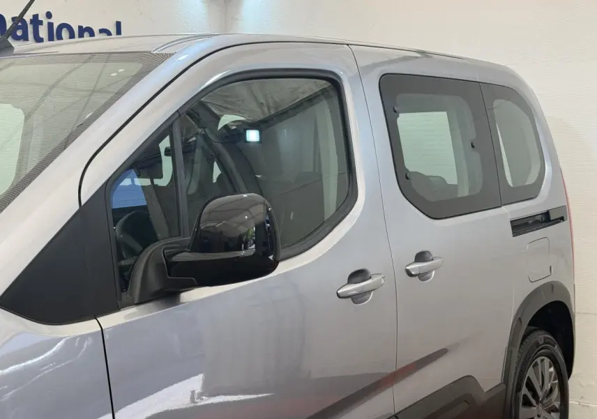 Vue côté gauche en gros plan sur le Peugeot Rifter gris clair, mettant en valeur la porte arrière coulissante et le rétroviseur noir.