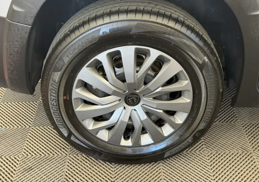 Gros plan sur la roue avant droite du Peugeot Rifter gris clair, avec jante à enjoliveur argenté et pneu Bridgestone.