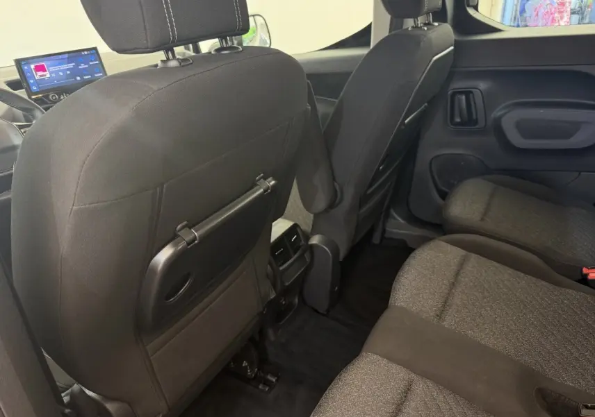 Vue intérieure arrière du Peugeot Rifter gris clair 2024, montrant les sièges tissu et tablette rabattable au dos des sièges avant.