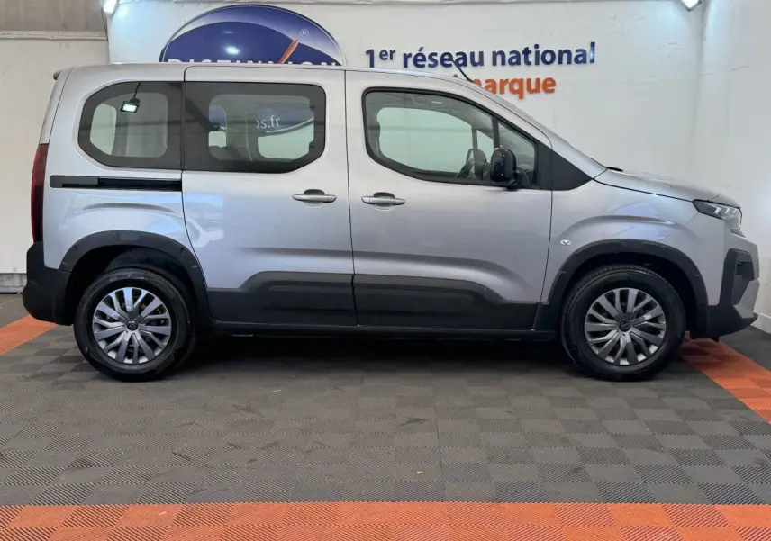 Vue de profil côté gauche d’un Peugeot Rifter gris clair 2024 avec vitres arrière teintées et jantes alliage.