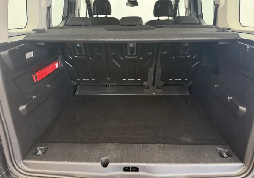 Coffre ouvert vu de l'arrière d'un Peugeot Rifter gris clair avec banquette arrière et cache-bagages visibles.