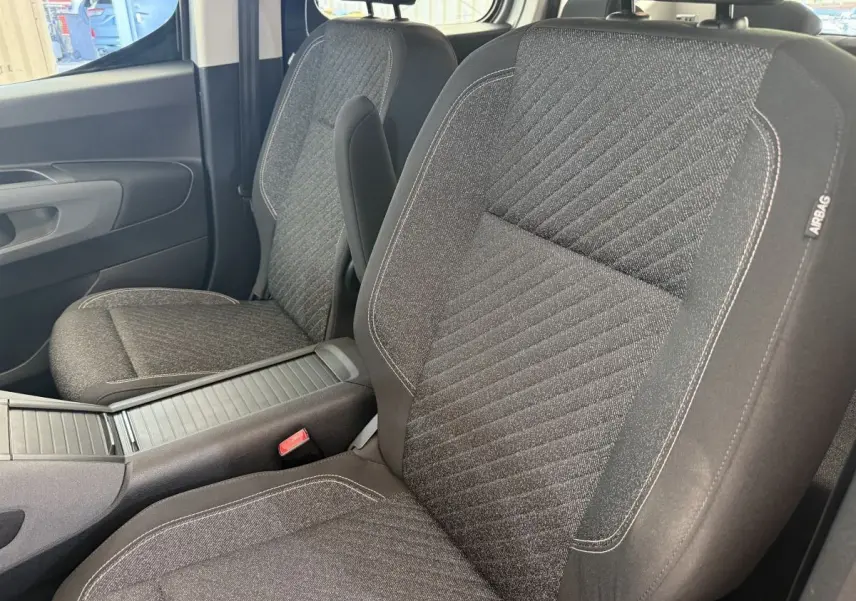 Vue rapprochée des sièges avant gris foncé du Peugeot Rifter 2024 avec accoudoir central et étiquette airbag.