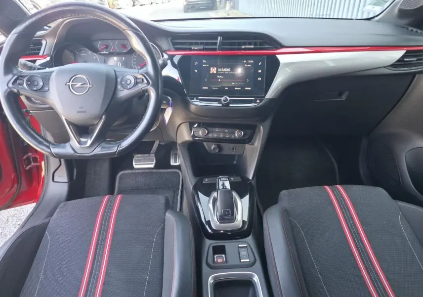 Vue intérieure avant de l’Opel Corsa rouge 2020, avec volant cuir, écran tactile central et sièges sport noirs à bandes rouges.