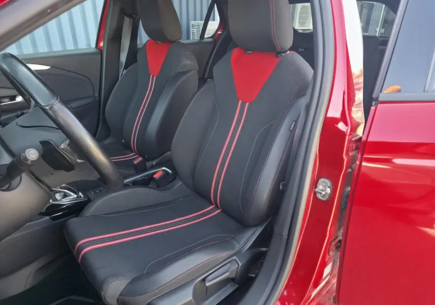 Vue intérieure côté conducteur d'une Opel Corsa rouge, sièges sport noirs avec surpiqûres et inserts rouges.