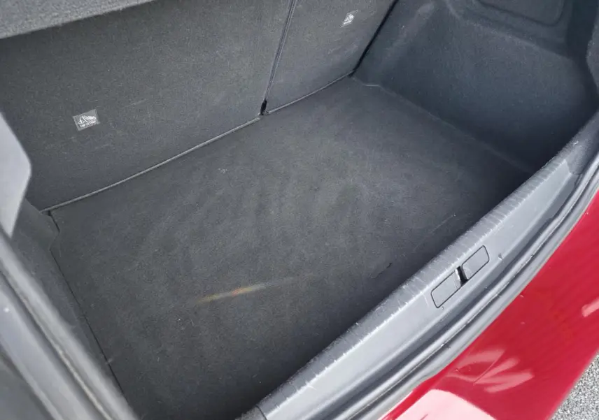 Coffre ouvert vu de dessus d’une Opel Corsa rouge, montrant le tapis de sol noir et l’intérieur spacieux.