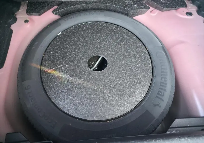 Roue de secours 16 pouces dans le coffre d'une Opel Corsa rouge, vue plongeante sur le pneu Continental.