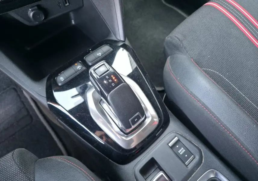 Gros plan sur la console centrale noire brillante de l'Opel Corsa rouge, avec levier de boîte auto et bouton mode conduite.