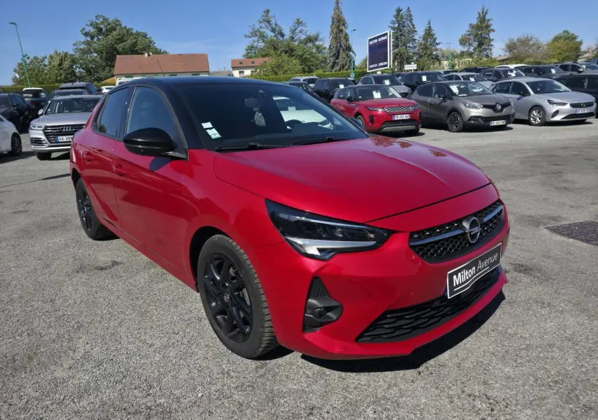 Opel Corsa rouge vue 3/4 avant droit avec toit noir et jantes alliage noires sur parking.