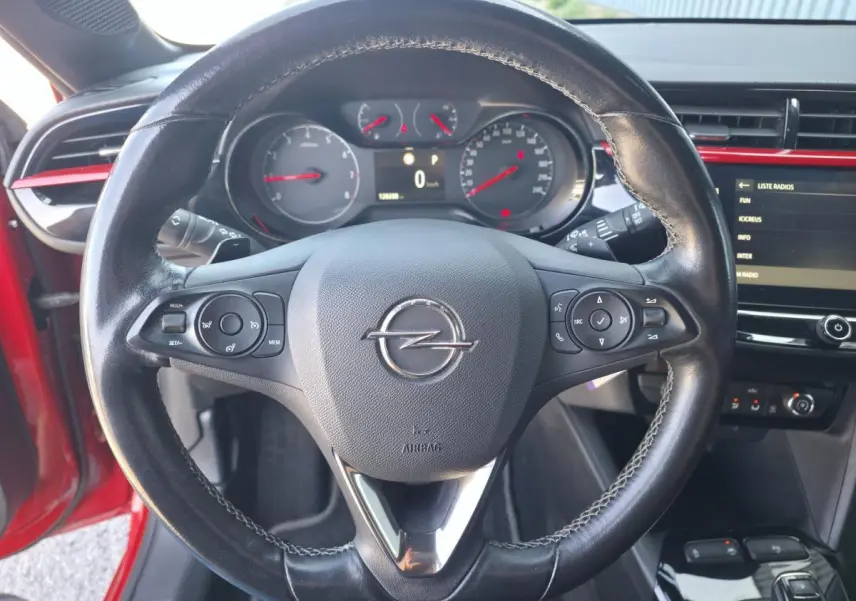 Vue intérieure centrée sur le volant en cuir noir de l'Opel Corsa rouge, avec tableau de bord et écran tactile visibles.