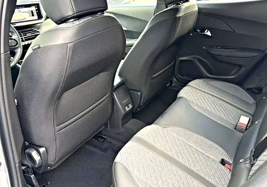 Vue intérieure arrière droite du Peugeot 2008 2025 gris artense, montrant les sièges arrière en tissu embossé et les dossiers avant noirs.