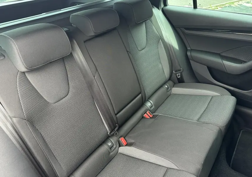 Vue latérale des sièges arrière noirs en tissu de la Skoda Octavia Combi 2024, avec appuie-têtes et ceintures visibles.