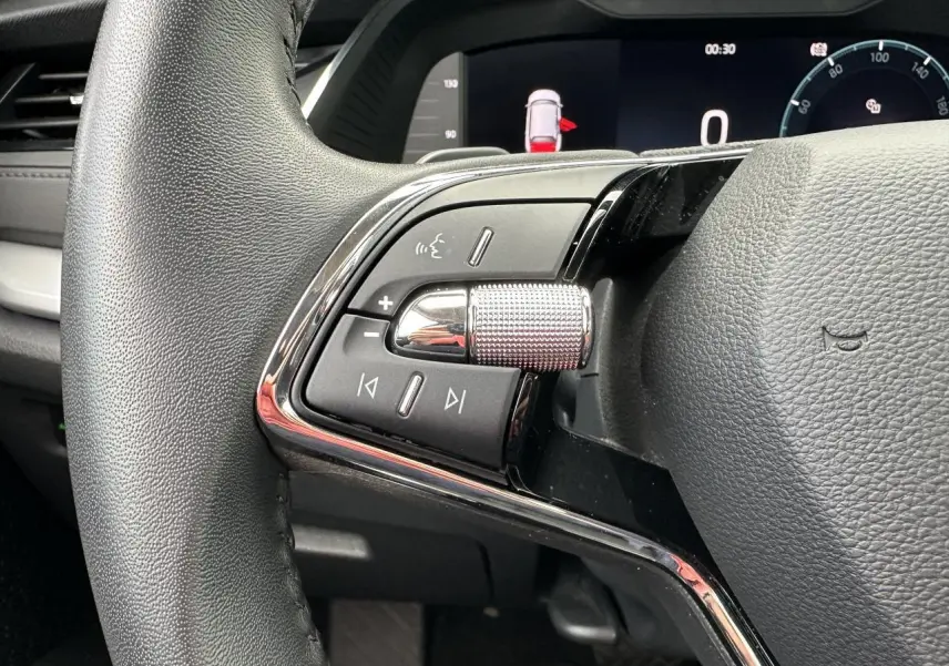 Gros plan sur les commandes gauche du volant cuir de la Skoda Octavia Combi gris graphite, tableau de bord numérique visible.