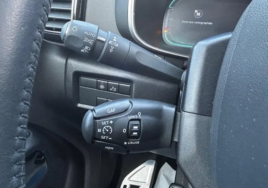 Gros plan sur les commandes de régulateur de vitesse et éclairage côté gauche du volant d'un Citroën C5 Aircross gris platinium.