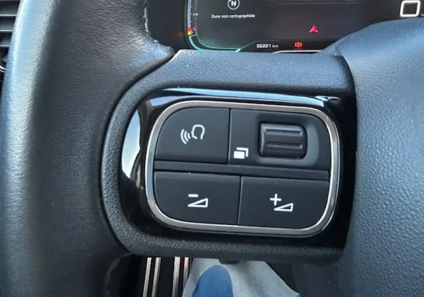 Gros plan sur les commandes au volant noir et chrome du Citroën C5 Aircross gris platinium, affichage numérique en arrière-plan.