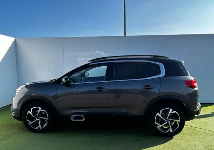 Profil côté gauche du Citroën C5 Aircross gris platinium métallisé avec jantes alliage 18 pouces et barres de toit noires.