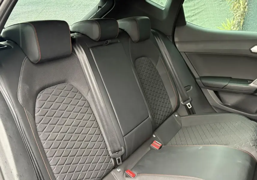 Vue latérale des sièges arrière noirs avec surpiqûres rouges du SEAT LEON 2024, finition FR, intérieur élégant.