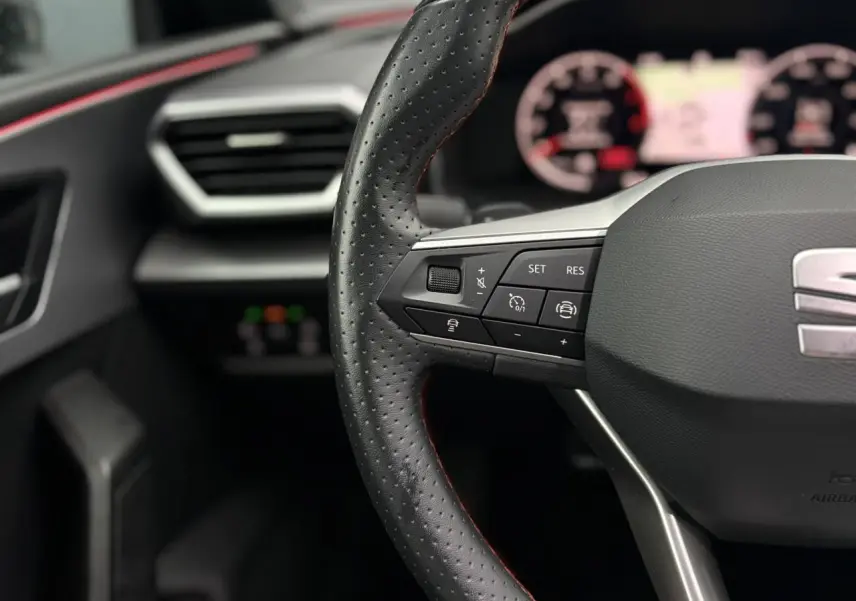 Gros plan sur le volant cuir perforé avec commandes multifonctions du SEAT Leon 2024, ambiance intérieure sombre.