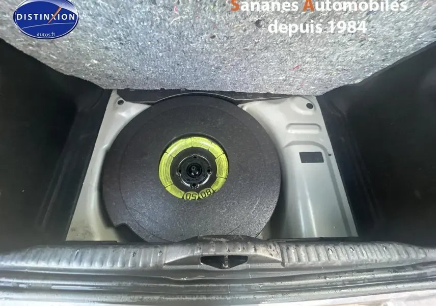 Vue plongeante sur la roue de secours galette dans le coffre d'une Citroën C3 gris foncé 2023.