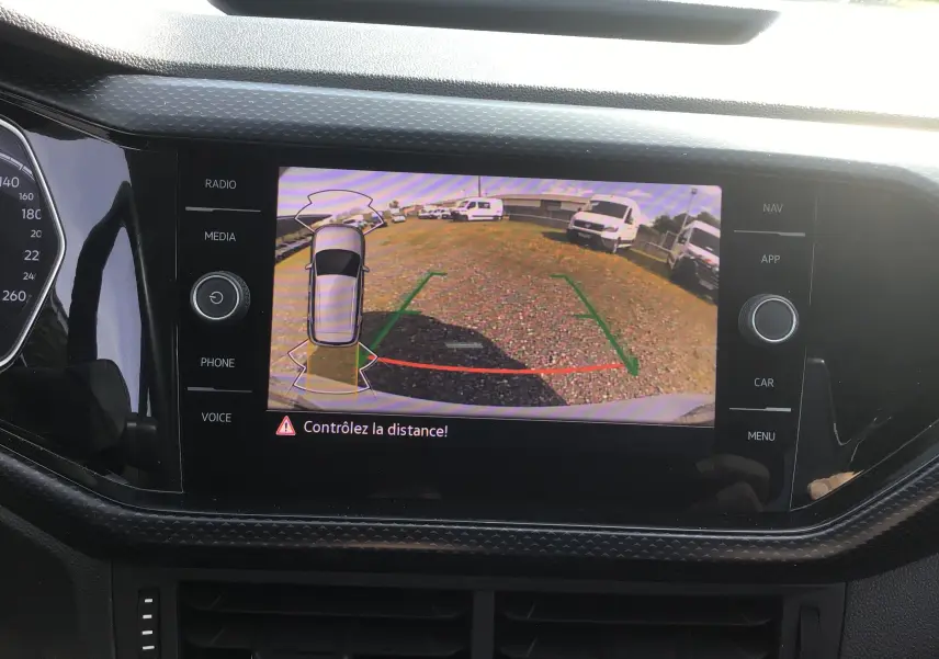 Vue intérieure sur l'écran de la caméra de recul du Volkswagen T-Cross blanc, affichant les lignes de guidage et l'alerte de distance.