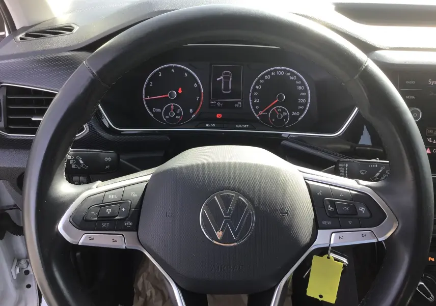 Vue rapprochée du volant noir du Volkswagen T-Cross blanc 2021, avec commandes intégrées et tableau de bord digital.