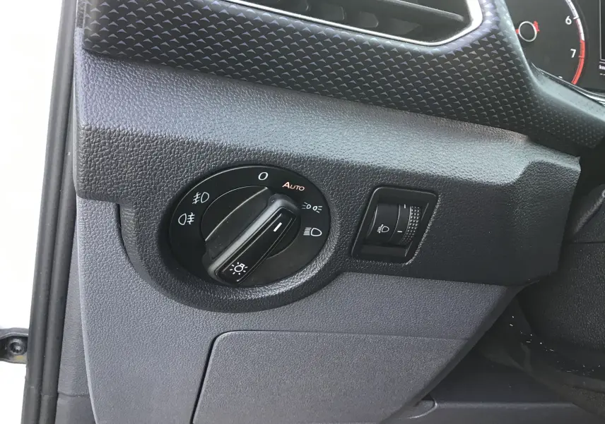 Détail du tableau de bord côté gauche du Volkswagen T-Cross blanc 2021, avec commande des phares et réglage du faisceau lumineux.