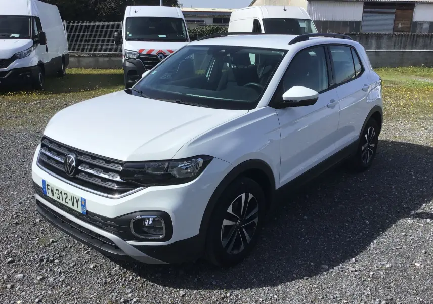 Volkswagen T-Cross blanc en 3/4 avant droit, avec jantes alliage et barres de toit noires visibles.