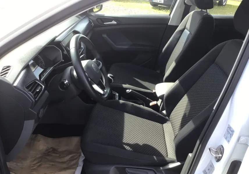 Vue intérieure côté conducteur du Volkswagen T-Cross blanc 2021, montrant les sièges avant et le volant avec boîte manuelle.