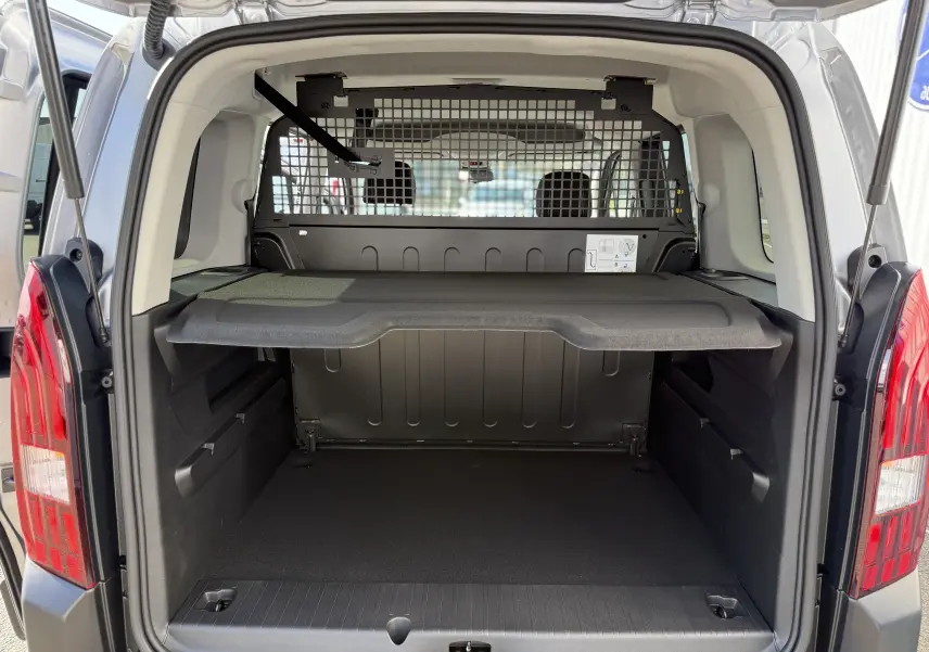 Vue arrière du coffre ouvert du Peugeot Rifter gris acier, montrant la séparation grillagée et la tablette de rangement.