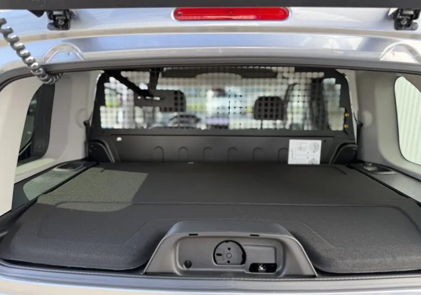 Vue arrière ouverte du coffre du Peugeot Rifter gris acier, avec séparation grillagée visible entre l'habitacle et le coffre.