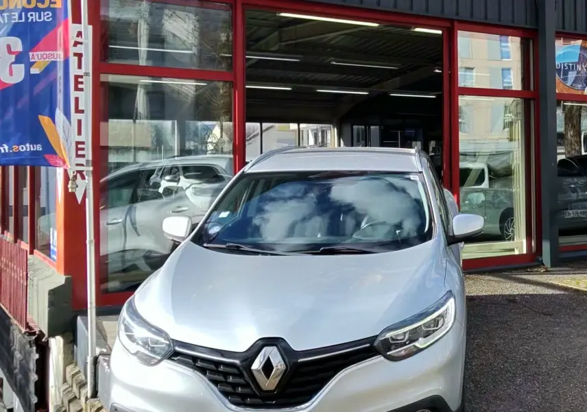 Renault Kadjar gris platine vu de face, stationné devant un garage avec enseigne AD Expert.