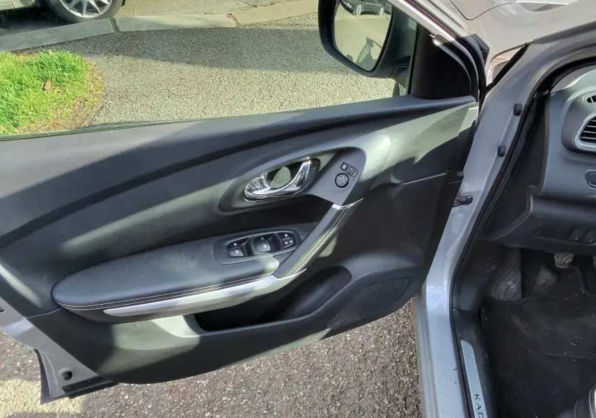 Vue intérieure côté gauche de la porte avant ouverte d’un Renault Kadjar gris platine, avec commandes de vitres et seuil marqué Kadjar.