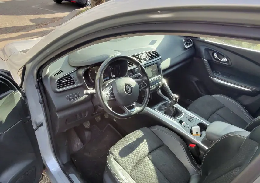 Vue intérieure côté conducteur du Renault Kadjar gris platine, montrant le volant cuir, la console centrale et la boîte manuelle.