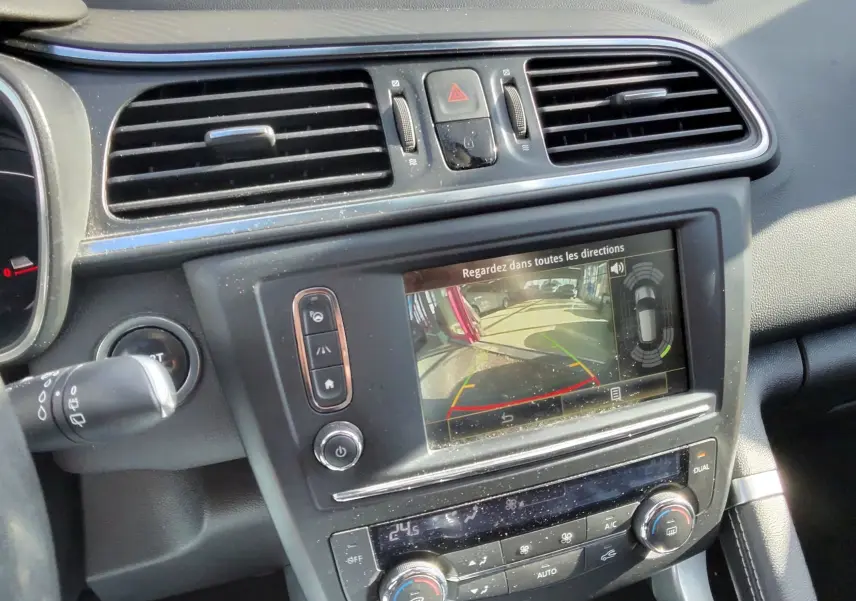 Vue intérieure du tableau de bord du Renault Kadjar gris platine, avec écran de caméra de recul et commandes de climatisation visibles.