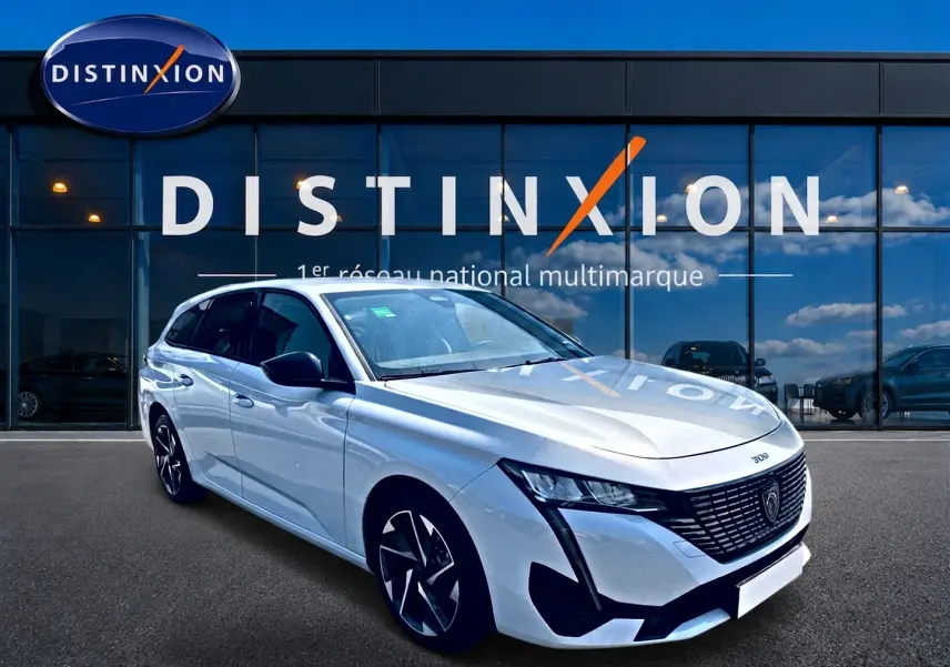 Peugeot 308 SW blanche vue en 3/4 avant droit, avec jantes alu et calandre noire distinctive devant un showroom Distinxion.